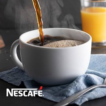 Fresh coffee poured into a white ceramic mug on a dark table, with a glass of orange juice behind it