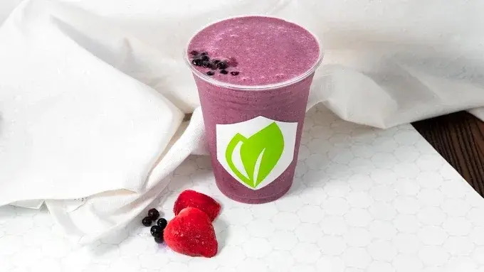 A berry smoothie in a branded Fit For Life cup, with fresh blueberries and strawberries alongside